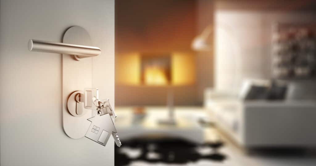 Clés de maison avec porte-clés maison accrochées à une serrure de porte, révélant un salon moderne et chaleureux en arrière-plan flou.