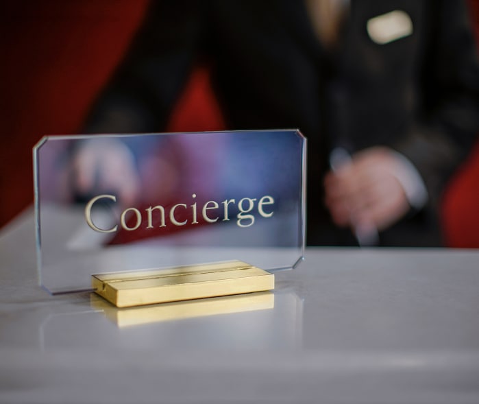 Signe Concierge doré sur bureau d'accueil, avec un professionnel de l'hôtel en arrière-plan flou.