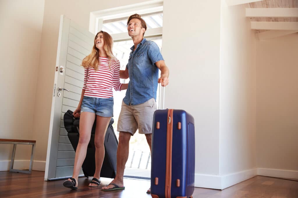 Couple souriant arrivant dans une maison de vacances avec leurs valises, regardant vers le haut, heureux de commencer leur séjour.