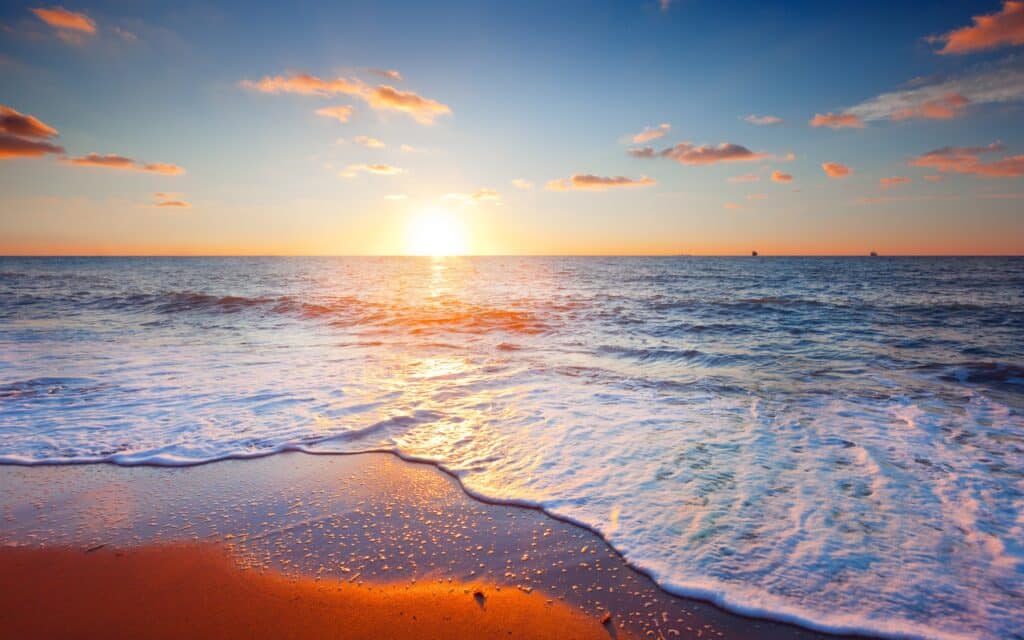 Soleil éclatant se couchant sur l'horizon marin, inondant l'océan de reflets dorés. Vagues moussantes sur le sable mouillé.